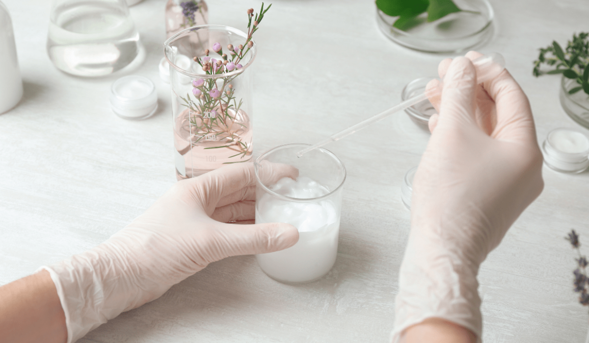 Un científico que lleva equipo de protección personal utiliza un gotero para tomar muestras de solución de un vaso de precipitados.