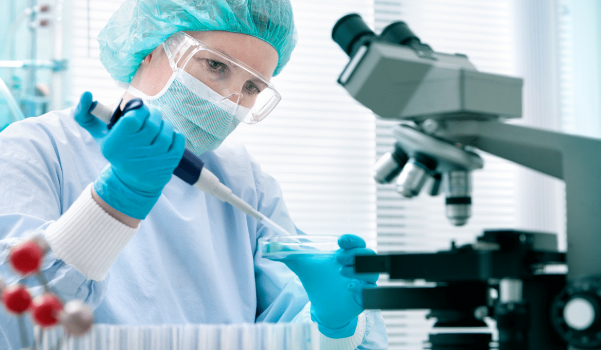 Un trabajador de biotecnología usa equipo de protección personal y dispensa una solución en una placa de Petri usando una pipeta.