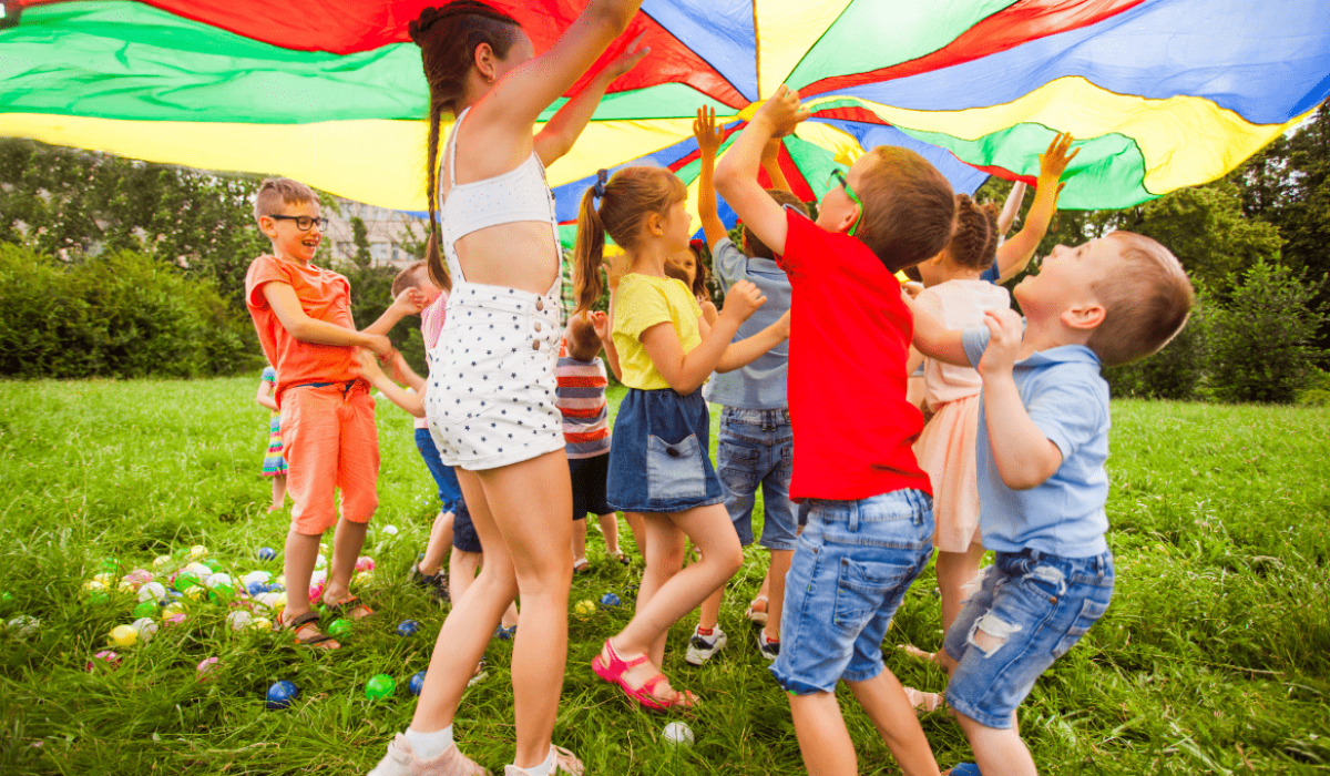 Los niños juegan en grupo con una variedad de juguetes y un paracaídas.