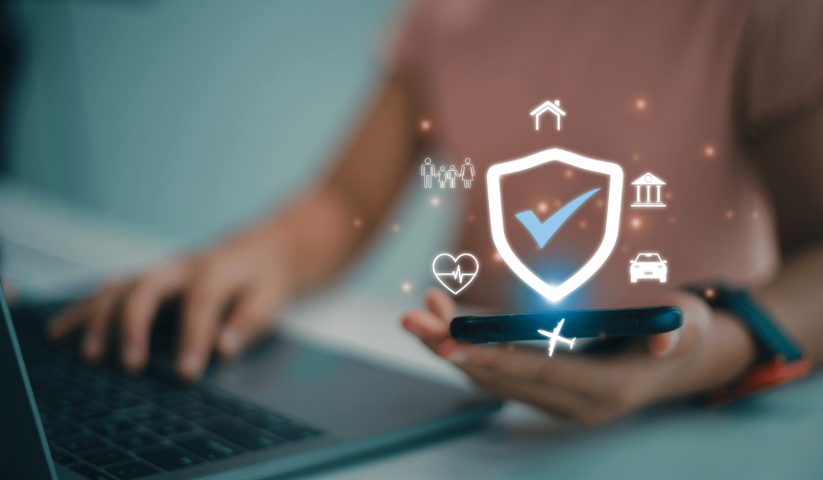 Una persona inicia sesión en una computadora mientras sostiene un teléfono con varios íconos de seguridad mostrados encima del teléfono.