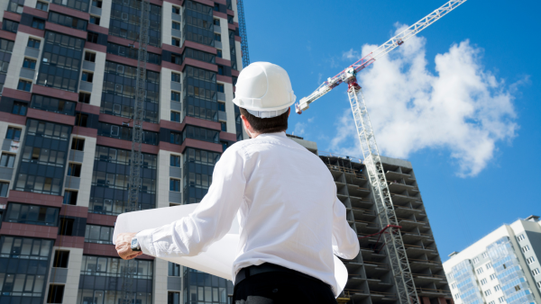 Arquitecto mirando su obra en construcción con unos planos en las manos 